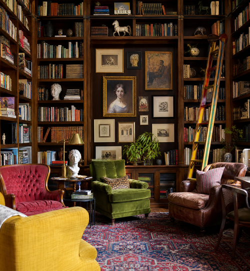 Eclectic library with floor-to-ceiling bookshelves, a colorful ladder, and vintage chairs.